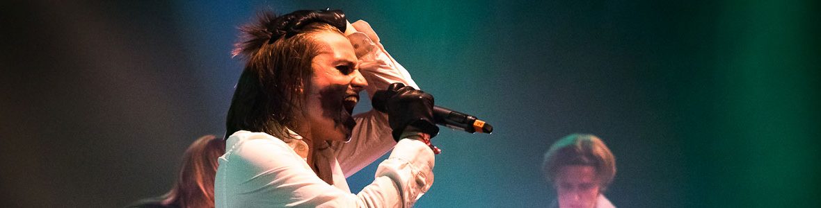 Sänger eines Auftrittes des local heroes Musikpreis Ein junger Mann singt kräftig in ein Mikrofon in seiner Hand. Er hat auffälliges Make Up für den Auftritt aufgetragen.